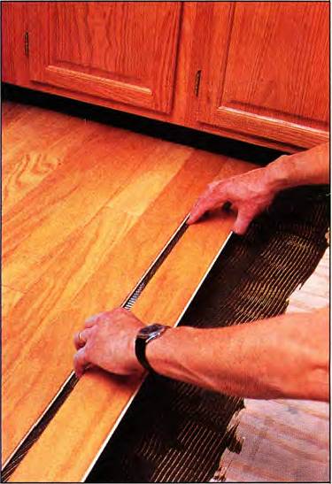 Person installing wood flooring with adhesive and a high-wear topcoating