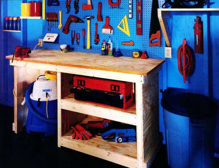 2-feet deep by 6-feet wide garage workbench with shopvac storage space on the left, and two shelves on the right for storing hand and power tools. On the backwall there is a pegboard tool wall with hand tools easily accessible and several shelving units in between the exposed wall studs.