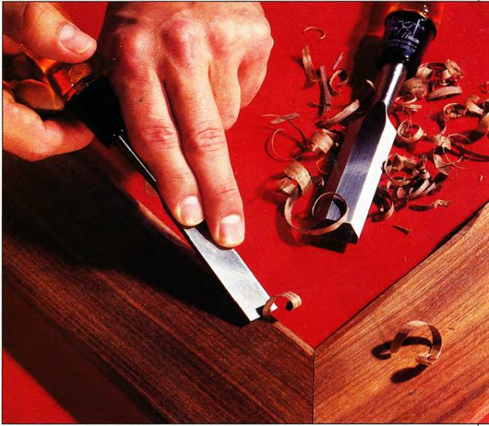 man chiseling edge of an almost-finished wooden workpiece