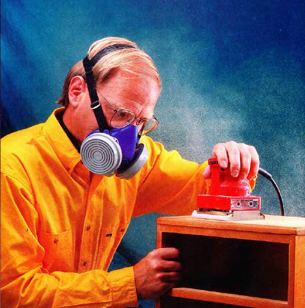 a man uses a respirator while sanding a side table