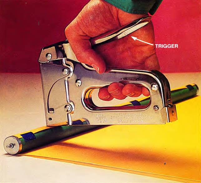 male hand pressing the trigger and using a staple gun to fasten a roller shade